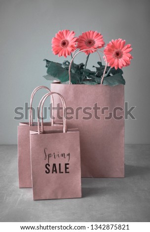 Coral gerbera daisy flowers and craft papper shopping bags on neutral background. Springtime sale concept image with text "Spring sale" on the bag