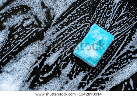 Blue sponge with beautiful divorces with foam close-up on a black glass background. Top view.