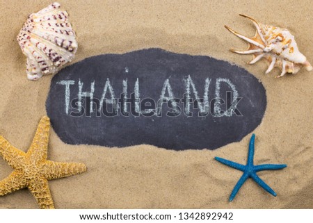 Handwritten word THAILAND written in chalk, among seashells and starfishes. Top view