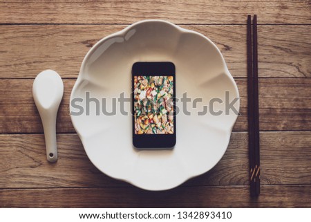 Mobile phone with food picture on screen in a plate on wooden table with chopsticks and spoon, Technology consumption.