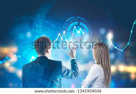Rear view of young businessman in glasses and blonde businesswoman working with graph and hud interface over blurred city background. Toned image double exposure