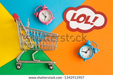 Flat lay of shopping cart and lol text in speech bubble with alarm clocks against colorful background minimal creative concept.