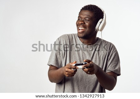 Cheerful man of African appearance with headphones and then in the hands of the game console a gray background of a video game