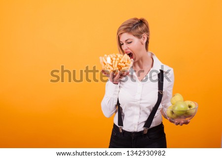 Attractive young woman looking at those yammy corn puffs over yellow background. White shirt. Blonde short hair.