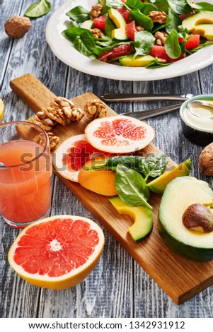 Avocado, grapefruit, spinach and walnut salad with tasty olive oil and lemon dressing, grapefruit fresh juice, ingredients on a board, served  in a white plate, on a blue wooden table, vertical