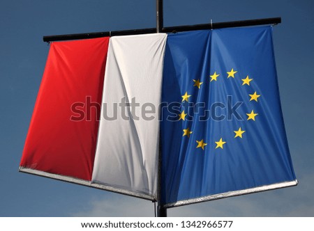 Flag of Poland and flag of European Union hang vertically on pole, next to each other, in background blue sky