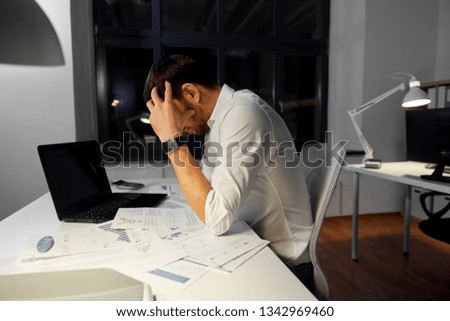 business, deadline and stress concept - stressed businessman with papers and laptop computer working at night office