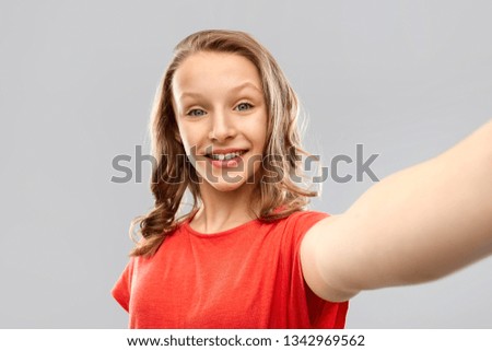 technology and people concept - smiling young woman or teenage girl in red t-shirt taking selfie over grey background