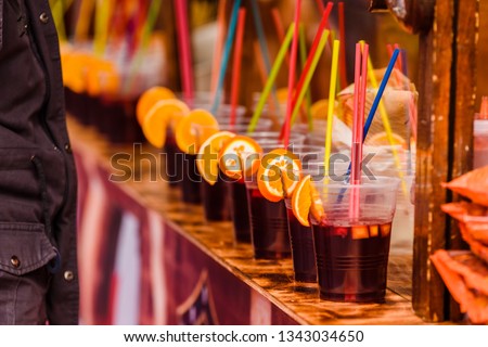 Plastic cups with refreshing alcoholic drinks with orange slices and colored straws at a summer festival.