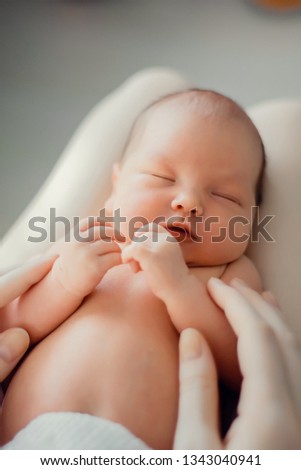 A newborn baby lies on the mother's lap. Mother holds her newborn baby. Woman relaxing in a white bedroom. Family at home