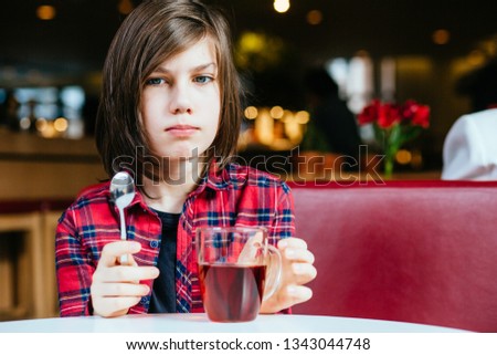 Close up portrait of teenager boy drinking tea sitting on red couch having breakfast in cafe interior.