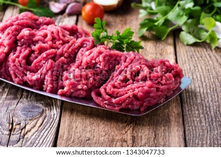 Minced beef, raw ground meat with cooking ingredients on rustic wooden table, close up, selective focus