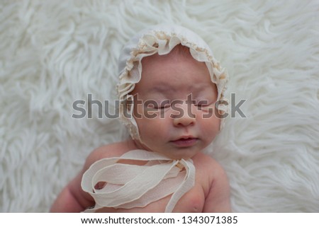 Newborn baby girl in a white milk cap is lying on the creme fur. Infant. Baby shower. 