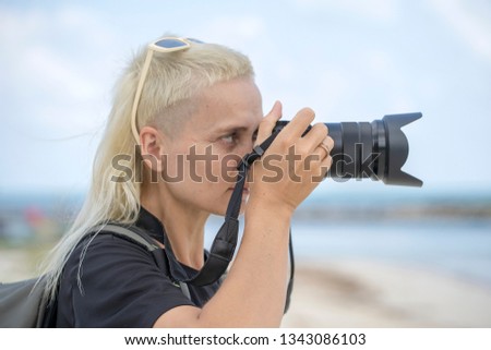 Tourist traveler photographer taking pictures of landscape on photo camera , hipster girl with backpack enjoying beautiful sea landscape. Close up portrait young blonde girl with backpack on the beach