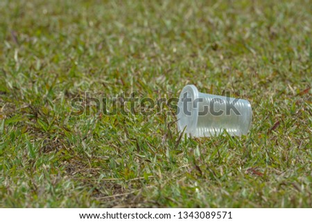 Used water plastic cup on green grass field at park.