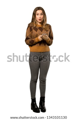A full-length shot of a Teenager girl with brown sweater surprised and sending a message over isolated white background