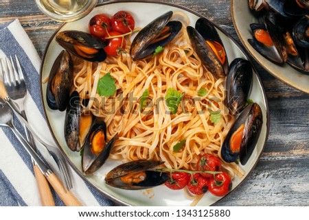 Pasta Mussels with herbs and tomatoes in a bowl. Seafood.  Dark wooden background. Top view. Flat lay
