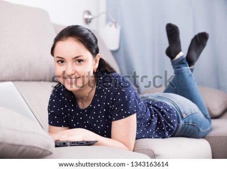Brunette woman relaxing with laptop while lying on sofa at home