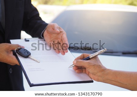 The new car owner signs the lease agreement, contract to receive the key.  