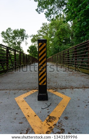 A trail bollard with caution markings on the Atlanta Beltline keeping dangerous vehicles from driving on pedestrian pathway
