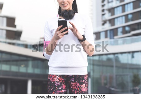 Cropped photo of  brunette in sportswear with big headphones typing on her mobile phone and searching for her music playlist for exercising, Apps and technology of new generation concept