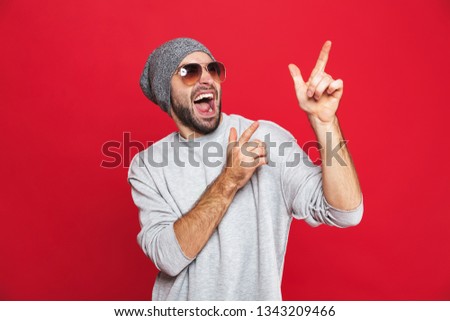 Image of cheerful man 30s in sunglasses laughing and pointing fingers aside isolated over red background