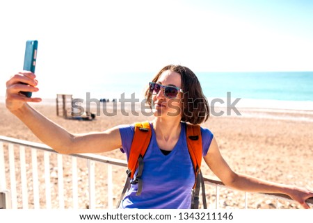 A girl takes a selfie on the waterfront. A woman walks through the resort town and takes pictures. Brunette travels around the Turkish city. Photo on the background of the sea.