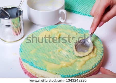 A woman lubricates the cakes and puts in a pile. Round wafer cakes of different colors. For making waffle cake. Nearby there is a can of condensed milk to soak the cakes.