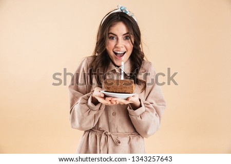 Image of beautiful excited young pretty woman posing isolated over beige background wall holding holiday cake.