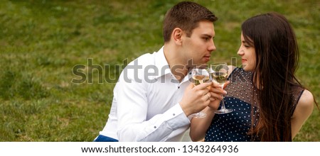Close up photo of romantic couple in love drinking wine and looking to each other on green grass background. banner for website