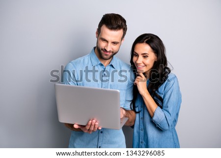 Portrait of charming inspired students using electronic devices watching videos browsing sites social networks isolated dressed in blue denim clothing on gray background