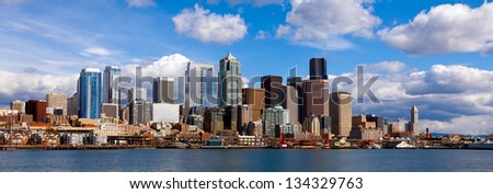 Panoramic view of Seattle waterfront and downtown buildings on a bright day with sun and clouds