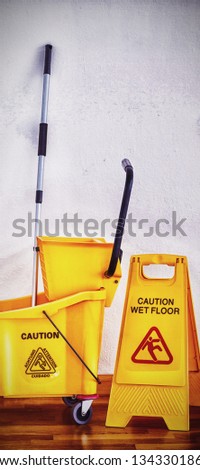 Yellow sign board with mop bucket on wooden floor against wall