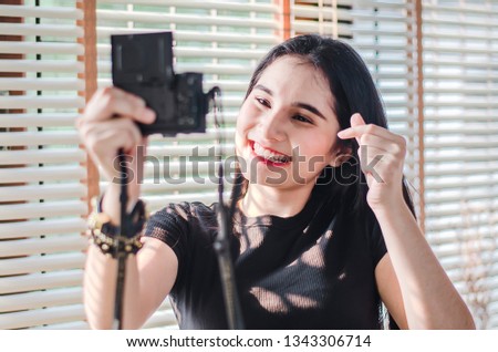 Beautiful girl standing in the room and taking selfie video for fashion blog. Woman holding compact camera in her hand and taking photo.