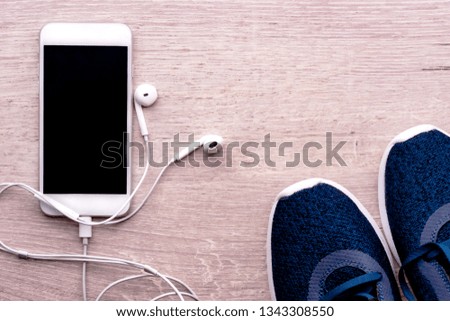 White smartphone with headphones connected on a wooden background next to sports shoes. Healthy lifestyle concept, fitness