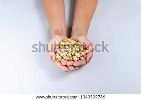 Pistachio. Female hand holding pistachio leaning against gray background.