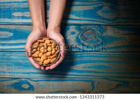 Brunette model holding pot of ceramic with natural almonds, blue wooden background.