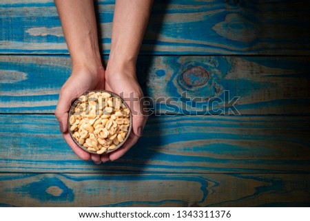Brunette model holding ceramic pot with roasted peanuts on blue wooden background.