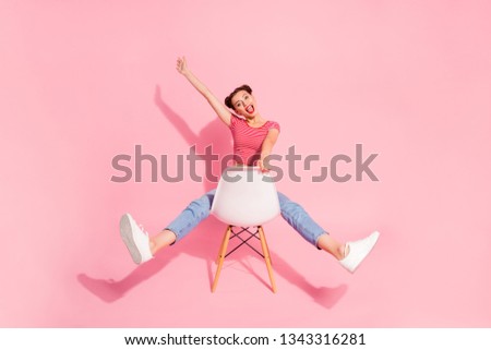 Nice attractive glamorous lovely adorable shine cheerful cheery optimistic girl wearing striped tshirt jeans sitting on chair having fun raising hand up isolated over pink pastel background