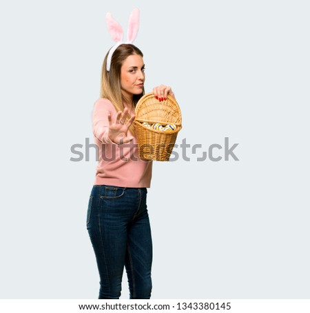 Young woman wearing bunny ears for Easter holidays is a little bit nervous and scared stretching hands to the front on isolated grey background