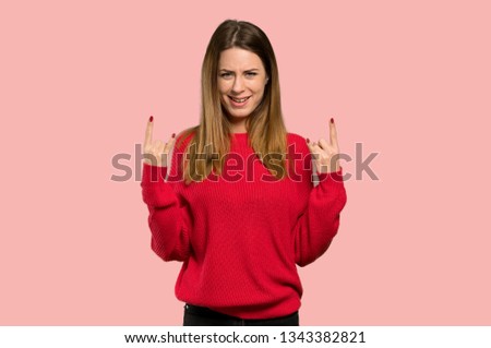 Young woman with red sweater making rock gesture over isolated pink background