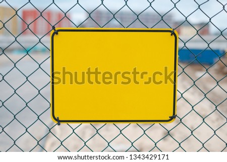 blank yellow sign on construction site fence - warning sign mockup