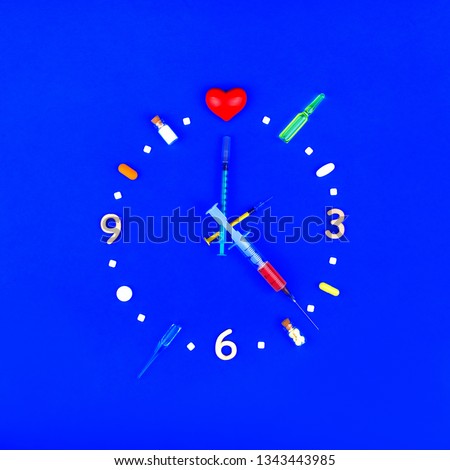 Medical pharmaceutical concept. Watch from tablets, ampoules and syringes. Medication time on a blue background. The idea of helping patients with heart disease. Heart Clock