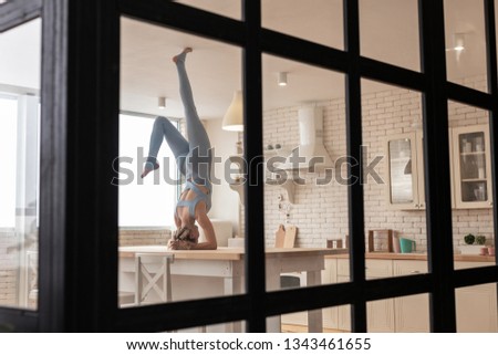Magnificent possibilities. Playful athletic girl standing on her head in kitchen while being all alone in apartments