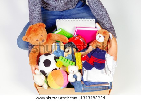 Donation concept. Kid holding donate box with clothes, books, school supplies and toys, white background
