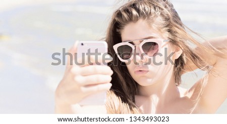 Portrait of a pretty teenage girl with long hair and sunglasses taking self portrait with her smartphone and enjoying her time on the beach