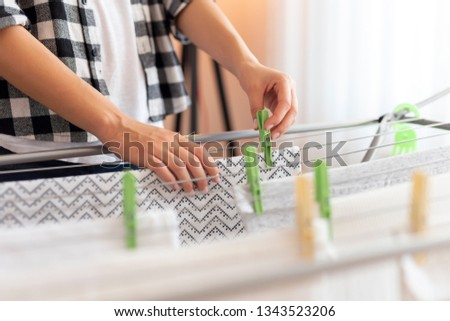Detail of female hands hanging the washing out to dry on a drying rack; woman hanging wet clothes on a drying rack with clothes pins