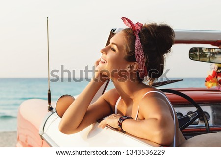Beautiful and happy woman is wearing bandana driving retro cabriolet car Royalty-Free Stock Photo #1343536229