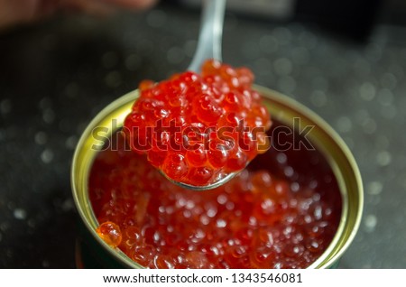 large granular caviar of salmon fish in a jar with a spoon in his hand close-up
