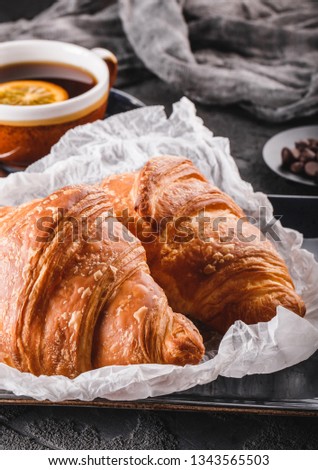 Breakfast with fresh french chocolate croissants on paper over dark background with napkin and cup of tea. Dessert, puff pastries, top view